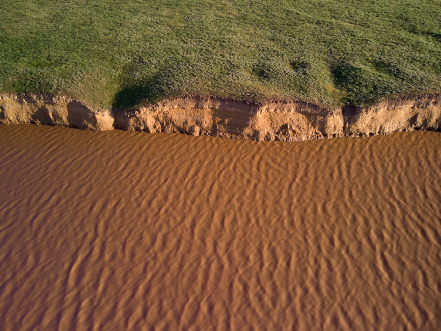 Aerial view of river bank being eroded and sediment in water.
