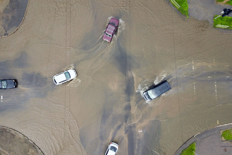 Cars driving through dirty water on flooded road.