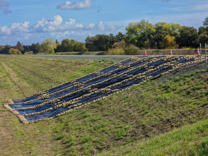 Erosion control blankets and sandbags places on steep grassy embankment.